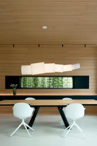 Modern dining room with white chairs and wood table, featuring a unique ceiling lamp and a window with greenery.