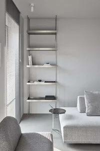 A modern interior design featuring minimalist metal shelving unit against a gray wall and a gray sofa with a side table.