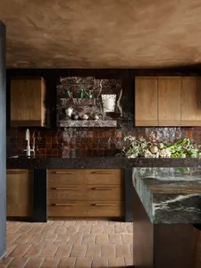 A modern kitchen with granite countertops, wooden cabinets, and dark tiles.