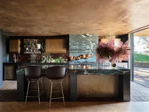 A modern kitchen with a marble countertop and island, featuring wooden cabinets and a view of the outdoor area.
