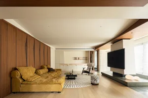 A modern living room with a wooden floor, a yellow sectional sofa, and a large television on a platform.