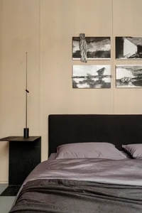 A minimalist bedroom with a bed featuring a textured fabric gradient and a black headboard, accompanied by abstract art piece