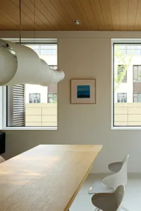 A modern minimalist dining room featuring wood furniture and plastic chairs.