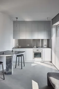 A modern minimalist kitchen with concrete countertops and white cabinetry.