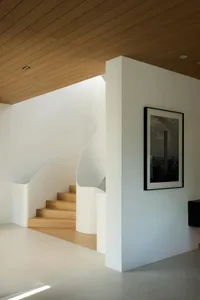 Modern minimalist staircase with curved white railings, wooden steps, and a concrete landing.