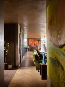 A modern residential living room with concrete ceiling and wooden flooring, featuring a green sofa and abstract paintings.