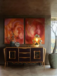 A warm, cozy living room featuring a wooden cabinet with a unique design, surrounded by vibrant artwork and a large potted pl