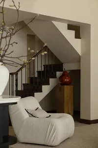 A cozy residential staircase with wooden steps and black railings, featuring a modern, plush armchair and a red pear sculptur
