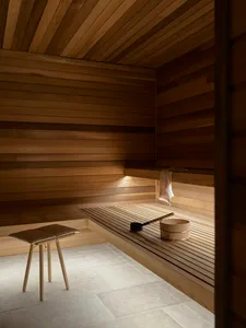 An industrial sauna room with wooden walls and benches, featuring a stool and a wooden bucket with a ladle.