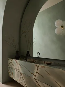 A sleek, modern bathroom featuring a marble vanity, cylindrical light fixture, and a large, arched mirror.