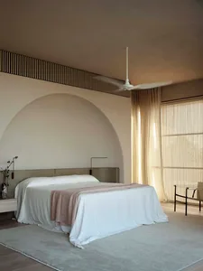A minimalist bedroom featuring a textured,loomed-cotton fabric on the bed, with a ceiling fan and a large window with blinds.