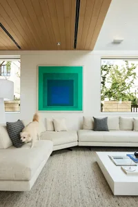A minimalist living room with neutral fabrics, concrete accents, and a green geometric artwork.