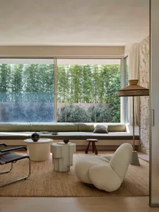 A cozy minimalist living room with a built-in sofa, fabric cushions, and stone accents, featuring floor-to-ceiling windows wi