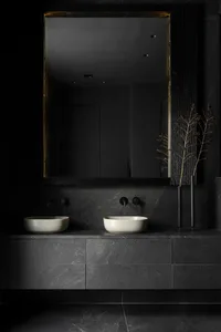 A modern bathroom with dark granite tiles, white vessel sinks, black fixtures, and a black-framed mirror.