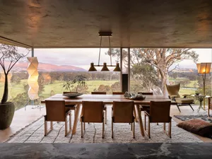 Modern dining room with a wooden table and chairs, large windows, and a view of the countryside.