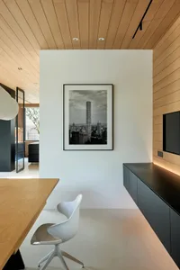 A home office with a modern design featuring a white chair and a wooden desk, with a black and white photograph of a cityscap