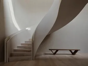 A modern interior with a sleek, curving staircase made of tukey wood. The space features minimalist design and light-colored 