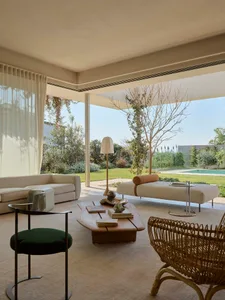 Modern living room featuring a woven armchair, fabric sofa, wooden table, and glass lamp. Bright, spacious, and contemporary.