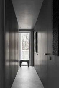 A modern minimalist hallway with concrete walls, a stone bench, and a large window at the end.
