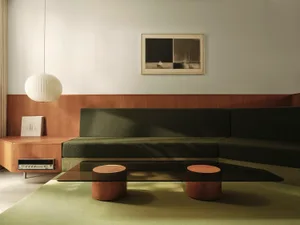 Modern green sofa with a glass coffee table and a wooden side table with a round lamp shade and a piece of art on the wall.