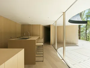 Modern kitchen with wooden cabinets and flooring, featuring a sleek island with a sink and countertop stools.