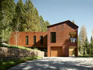 Modern residential house with metal siding, surrounded by trees with a gravel driveway.