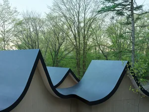 Modern metallic architectural design featuring curved, metal roofs surrounded by green trees.