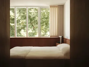 A minimalist bedroom featuring modern minimalistic elements, wooden headboard, fabric bedding, and glass elements.
