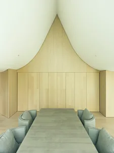 A modern interior space with minimalist design, featuring a wood paneled ceiling and a long, sleek dining table surrounded by