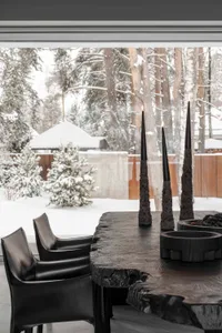 A cozy winter cabin scene with snow-covered trees, a black leather chair, and black candles on a wooden table.