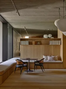 Contemporary wooden lounge area with concrete ceiling, white cushions, and round table and chairs.