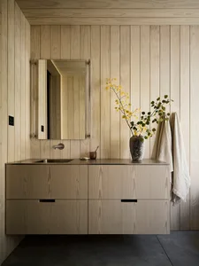 A minimalist bathroom with wooden cabinets, a steel faucet, and a vase with yellow flowers on a sink counter.