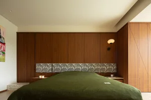 A modern minimalist bedroom featuring a wooden wall with a patterned upholstered headboard and green bedding.