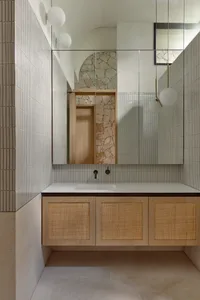 Modern bathroom interior with white textured ceramic tiles, floating wooden cabinet with woven wicker doors, and a minimalist