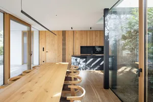 A modern kitchen dining room featuring wooden furniture, glass walls, and a minimalist design.