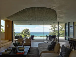 Modern living room featuring concrete walls and floor, beach view, and comfortable seating.