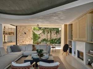 A modern living room featuring a large couch, coffee table, and chairs with a wooden floor and stone walls.