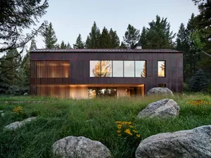 A modern metal-clad house exterior with large windows and a rustic wooden door.