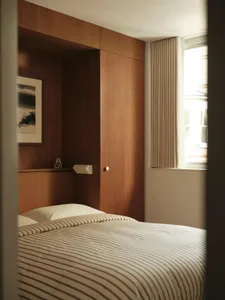 A modern minimalist bedroom featuring a wooden paneled wall, white bedding with gray stripes, and a window with beige curtain