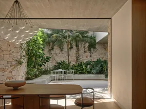 A modern minimalist patio with concrete and stone elements, featuring a small table and chairs under a covered area.