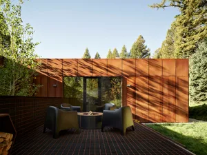 Modern patio area with metal roof and black grid flooring surrounded by trees.