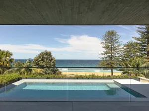 A modern swimming pool overlooking the ocean, surrounded by lush greenery and a concrete patio.