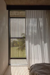 A bedroom interior featuring a transparent curtain, concrete walls, and modern lighting.