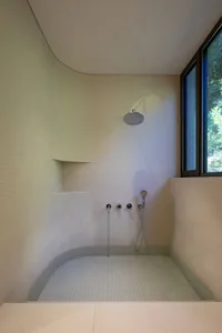 A minimalist bathroom featuring white tiled walls and floor with a walk-in shower area.