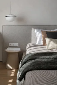 A minimalist bedroom with a bed, pillows, a blanket, and a side table with a book.
