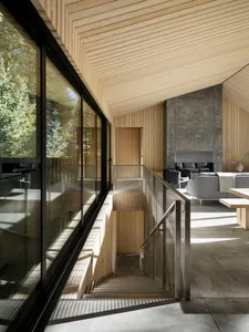 Modern minimalist interior design with wood, concrete, and glass materials in a cabin setting.