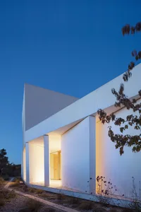 A minimalist white house with prominent white walls and a clear blue sky in the background.