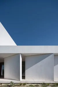 A minimalist house with a concrete exterior under a clear blue sky.