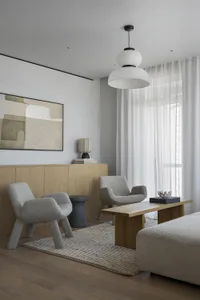 A modern minimalist living room with two gray armchairs, a wooden coffee table, and a wooden cabinet.