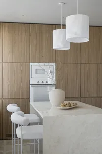 A modern residential kitchen with white marble countertops, wooden cabinets, and a white textured counter.